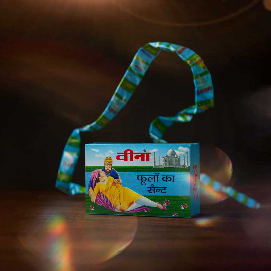 A long, continuous hanging strip of Veena Scent of Flowers traditional Indian attar packaging wrapped gracefully around the main display product box.