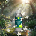 Veena Camphor Premium Vaporizer and Diffuser Oil 100ml bottle placed against a sunlit mystical forest background with falling white blossoms.