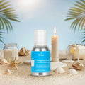 Veena Summer Breeze Fragrance for Candle Making bottle displayed on a sandy beach setting surrounded by scattered seashells, starfish, and burning white candles.