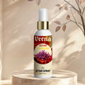 Veena Kesar Chandan premium attar spray 100ml bottle with a gold collar displayed on a round marble podium with soft branches and warm shadows.