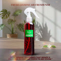 Veena Jasmine premium room freshener spray bottle displayed on a wooden surface with a soft-focus indoor houseplant background.