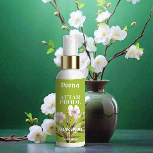 Veena Attar Phool premium attar spray 100ml bottle with a gold collar displayed in front of a ceramic vase filled with blooming white blossoms on a rich green background.
