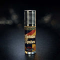 Veena Golden Ember premium non-alcoholic perfume oil roll-on bottle with a wavy retro-art label and ribbed silver cap against a dark bokeh background.