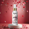 Veena Rose premium attar spray 100ml bottle with a gold collar displayed on a white round podium with falling red rose petals.