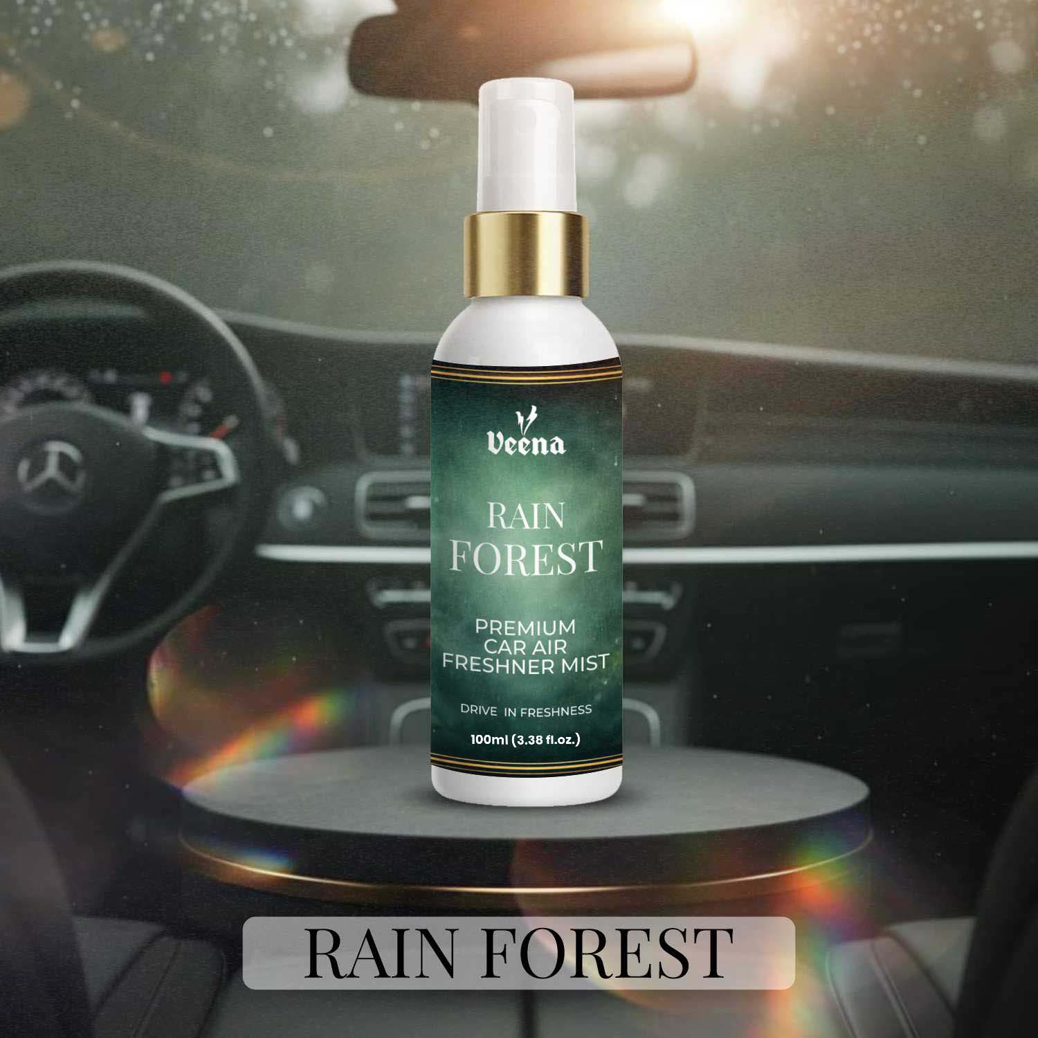 Veena Rain Forest Premium Car Air Freshner Mist 100ml bottle sitting on a sleek dark pedestal inside a modern steering-wheel dashboard environment.