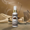 Veena Royal Oudh premium attar spray 100ml bottle with a gold collar displayed next to burning incense with swirling smoke plumes.