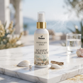 Veena Seaside Serenade Potpourri Spray 100ml bottle on a luxury marble table with seashells and an ocean beach background – Ocean Fresh Escape Room Freshener.