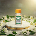 Veena Premium Attar Chameli 2ml miniature glass bottle standing on clean white marble podium surrounded by white jasmine flowers