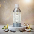 Veena Home Fragrances 500ml Coco Vanilla Fragrance Oil aluminum bottle on a marble stand surrounded by vanilla flowers, pods, and broken coconut shells.