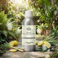 Veena Home Fragrances 500ml Lemongrass Fragrance Oil aluminum bottle on a garden pathway surrounded by fresh lemongrass stalks and sliced lemons.