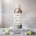 Veena Home Fragrances 500ml White Musk Fragrance Oil aluminum bottle on a marble slab surrounded by soft white feathers and delicate white roses.