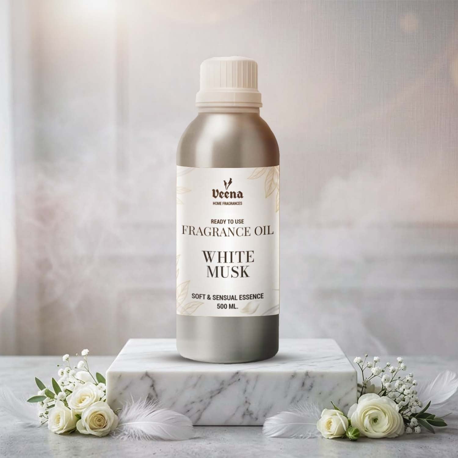 Veena Home Fragrances 500ml White Musk Fragrance Oil aluminum bottle on a marble slab surrounded by soft white feathers and delicate white roses.