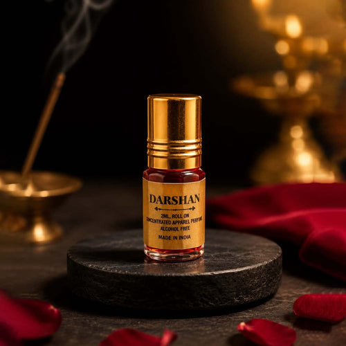 Darshan 2ml crimson perfume oil roll-on resting on a dark marble disc with red rose petals and an incense stick in the background.