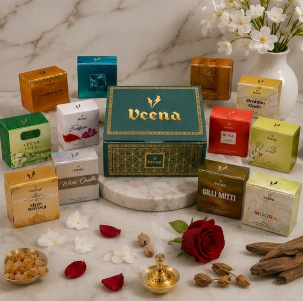 Veena signature emerald green luxury gift box surrounded by assorted colorful mini fragrance boxes including Gilli Mitti, White Oudh, and Mogra on a marble table.