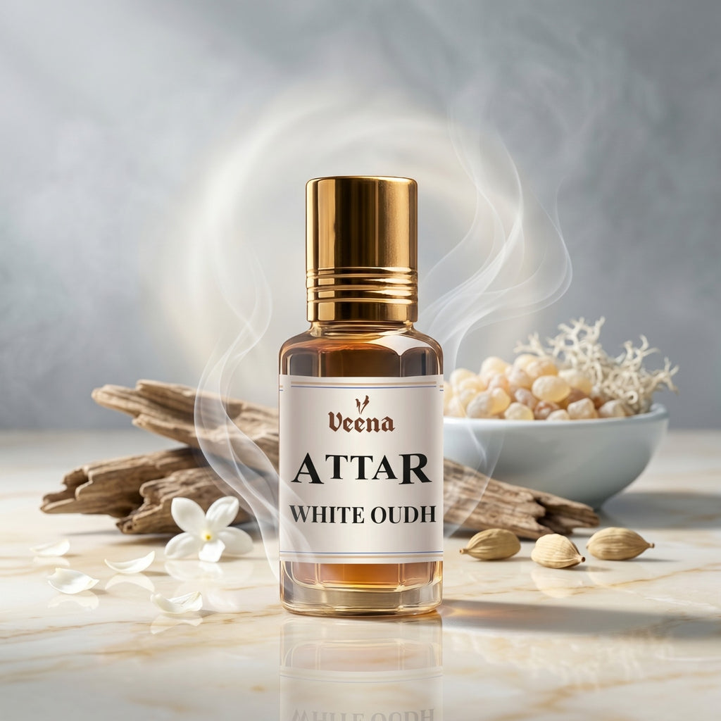 Veena Attar White Oudh premium concentrated fresh oud perfume oil bottle with a gold cap, set on a bright marble surface surrounded by natural agarwood pieces, cardamom, white petals, and delicate curls of aromatic smoke.