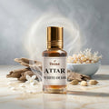 Veena Attar White Oudh premium concentrated fresh oud perfume oil bottle with a gold cap, set on a bright marble surface surrounded by natural agarwood pieces, cardamom, white petals, and delicate curls of aromatic smoke.
