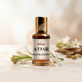 Veena Attar Rajnigandha premium concentrated tuberose perfume oil bottle with a gold cap, set on a polished white surface surrounded by fresh white Rajnigandha flowers, cardamom pods, and elegant curls of aromatic smoke.