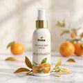 Veena Mandarin Potpourri Spray 100ml bottle displayed on a white marble table with fresh oranges and leaves – Bright Citrus Notes Home Fragrance.