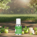 Veena Green Apple Fragrance for Candle Making bottle placed outdoors on a path surrounded by fresh green apples and lit candles under bright sunlight.