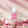 Veena Rose Fragrance for Candle Making bottle displayed on a round pink pedestal surrounded by scattered pink rose petals and burning white candles.