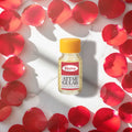 Veena Premium Attar Gulab 2ml miniature glass bottle standing on luxury white marble slab surrounded by red rose petals